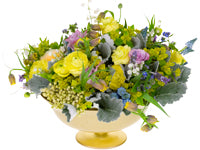 A delicate arrangement of Lily of the Valley, fritillaria, muscari, yellow runuculus, dusty purple roses, Forget-Me-Nots, butterfly lavender, euphorbia, brasilia, and dusty miller sits in a golden bowl.