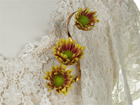 A brooch fashioned of curled copper aluminum wire supporting three red and yellow bi-color daisy mum blooms is fastened to a lacy white shirt.