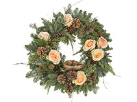 A holiday wreath enhanced with noble, cedar, and pine greens along with red twig dogwood branches, small pine cones, and pale peach rose blooms is adorned with a nest holding sphagnum moss and sweet gum pods.