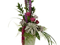An interesting vertical arrangement of tall purple liatrus, ruscus, lily grass, draped plumosa, bromeliad, Tillandsia, Brunia, hanging raspberry-colored amaranthus and matching roses.