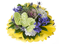 A bouquet of hydrangea, kale, antherium, delphinium, eryngium, and various foliage sits against a collar of scalloped yellow paper.
