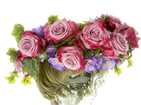 A robust floral crown of red and pink bicolor roses, faux ivy, and faux purple hydrangeas sits atop the short blonde hair of a mannequin head.