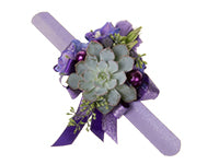 A purple wrist corsage features a single succulent centerpiece adorned with both dark purple and sparkly purple ribbons, seeded eucalyptus, lisianthus, eryngium, and delphinium.