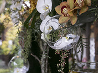 A garland of foliage adorned with white and Cymbidium orchids and a glass orb hangs over the edge of a roof on a historic building at Lan Su Garden.