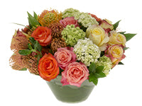 An arrangement of roses accompanied by chartreuse hydrangea, exciting pincushion protea blooms, and foliage.