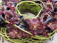 A table wreath fashioned from foliages and decorated with blooms, including orchids, calla lilies, and roses, in deep wine hues.