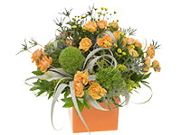 A centerpiece of orange spray roses, eryngium, green trick dianthus, baby chrysanthemums, tillandsia, solidaster, and ruscus in an orange square container.