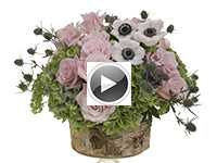 A round centerpiece of roses, sedum, hydrangea, eryngium, and anemone in a circular container wrapped in bark pieces.