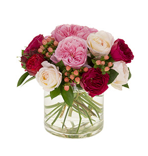 An arrangement of garden roses in deep red, playful pink, and soft white, accented with peach hypericum berries in a cylindrical glass vase.