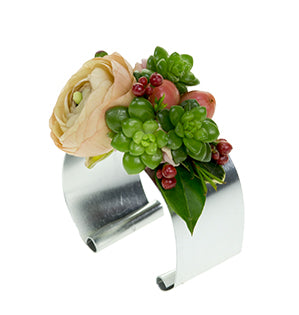A floral cuff fashioned of silver flat wire showcases a blush ranunculus bloom, some small bits of succulent, waxflowers, hypericum berries, and leaves of myrtle and oregonia.
