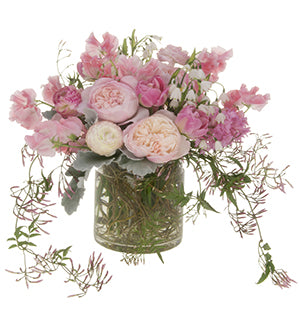A floral arrangement in a color palette of soft pinks features tulips, sweet pea, snowdrops, hyacinth, jasmine vine, dusty miller, garden roses, and curly willow.