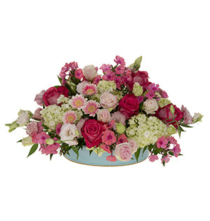 A lively centerpiece in oval design of mini hydrangea, roses in shades of pink, lisianthus, phlox, micro gerbera daisies, and Italian ruscus.