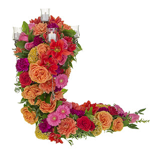 A dramatic candelabra centerpiece enveloped in Garden Roses, Dahlias, Cockscomb, and Gerbera Daisies in a vibrant polychromatic color palette of red, yellow, orange, pink, and purple, plus foliages of ruscus, Oregonia, and Salal.