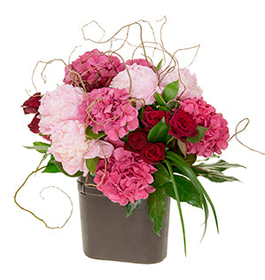 A bouquet of light pink peonies, hot pink hydrangea, and deep red roses with ruscus, fatsia, and lily grass, and accessorized with curly willow.