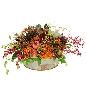 A round tin container holds an overflowing arrangement of cottage yarrow, Asclepias, pomegranates, decorative blackberries, spray roses, cockscomb Celosia, chocolate phlox, bunny tail, and orchids draping over the sides.