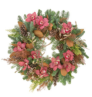 An evergreen wreath enhanced with magnolia leaves and cryptomeria is decorated with pink cymbidium orchids, magnolia buds on branches, and pine cones. 