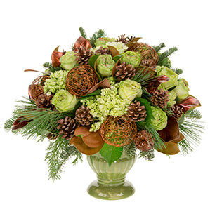 A festive green urn holds this elegant centerpiece of cedar, pine, and noble evergreens, plus leaves of magnolia, adorned with roses and hydrangea in chartreuse. Pine cones give a natural touch, and decorative orbs fashioned of copper wire add shine.