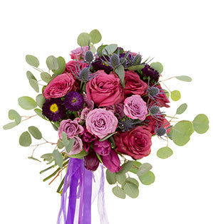 A bridal bouquet containing Blueberry roses, Eryngium, spray roses, China Aster in deep purple, magenta Tulips, and Silver Dollar Eucalyptus, tied in purple ribbons, creates a vibrant Ultra Violet palette.