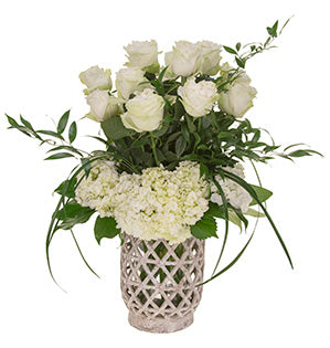 White roses and hydrangeas are accompanied by foliages of fatsia aralia, italian ruscus, and lily grass in a chic barrel lantern container.