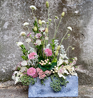 A vegetative style arrangement mixes a variety of materials like myrtle, elderberry, salvia, sedum, pink scabiosa.  astrantia, white scabiosa, and dried and preserved oak leaves.