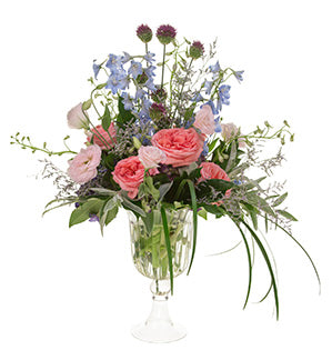 A floral arrangement of summer flowers including garden roses, hydrangea, delphinium, allium, lisianthus, misty, ruscus, fatsia, and lamb's ear in a glass compote.