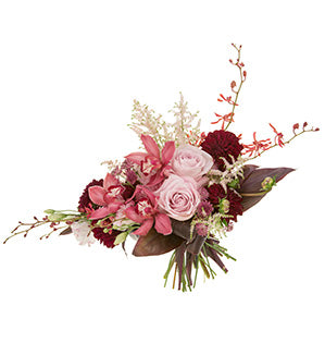 A bespoke garden style bouquet in blush and burgundy shades features garden roses, cymbidium orchids, astilbe, James Storie orchids, dahlias, astrantia, and ti leaves composing a horizontal line design.