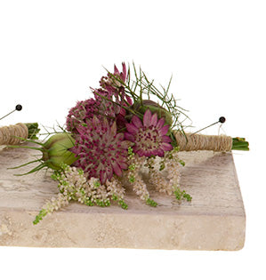 A floral boutonniere of astrantia and nigella is hand-tied with twine and rests on a tile slab.