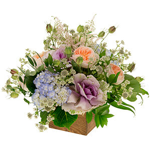 A combination of astrantia, astilbe, nigella, kale, hydrangea, luscious garden roses, fatsia, Italian ruscus, and Israeli ruscus arranged inside a wooden box create this rustic floral centerpiece.