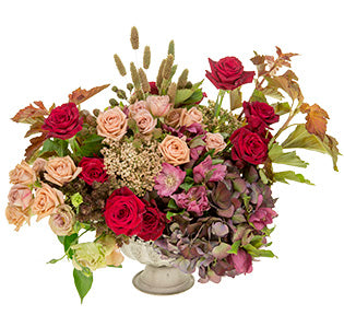 A bursting, textural centerpiece combines spray roses, lisianthus, berries, cottage yarrow, millet, hellebors, roses, hydrangeas, and nine bark in a rustic compote.