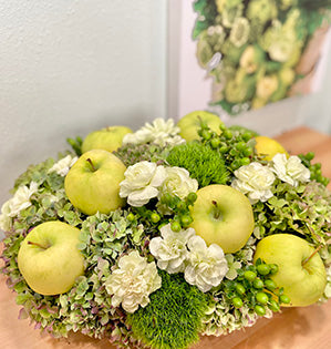 A floral centerpiece features green apples, hydrangeas, green trick dianthus, mini carnations, and hypericum.