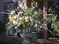 A lush urn design combines a variety of blooms in pastel shades with loose, reaching foliages.
