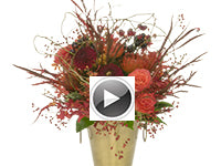 A wild hand-tied arrangement of willow tips, young rose hips, coral roses, orchids, yellow spray roses, orange pincushion, vibrantly colored peppers on a stem, deep red dahlias, red-stained grevillia, and a collar of fatsia leaves.