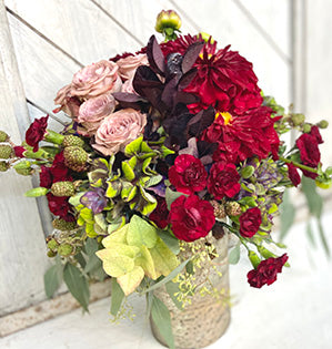 A hand-tied bouquet in burgundy, deep red and dusty pink colors features antique hydrangeas, dahlias, roses, and mini-carnations, blackberries, eucalyptus, and smokebush foliage.