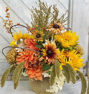 A floral arrangement is inspired by autumn flowers such as sunflowers, chrysanthemums, dahlias, autumn leaves, vines, pods and grasses in yellow and orange colors.