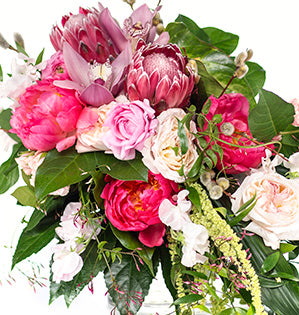 A gorgeous wedding bouquet in blush and pink hues is composed of garden roses, protea, peonies, and other beautiful blooms.