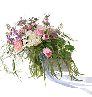 A beautiful Bespoke style hand tied bouquet mixes pink roses, white hydrangea, pink tulips, blue eryngium, purple freesia, seeded eucalyptus, and other foliages, and is tied off with a pale blue ribbon.