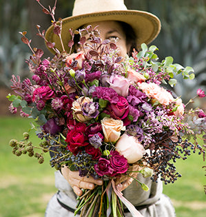 A beautiful rustic wedding bouquet mixes a variety of flowers and foliage in a pink, purple, and red color palette.