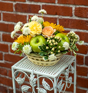 A vintage container is paired with sunflowers, garden roses, hypericum, scabiosa, variegated pittosporum, and Granny Smith green apples for an accent.