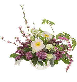 A bespoke garden style centerpiece featuring flowering cherry blossom branches, Love Lies Bleeding, lilacs, poppies, lisianthus, salal, fatsia, and dusty miller.