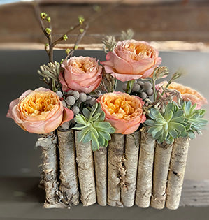 A contemporary design combines beautiful and elegant garden roses with rustic woodlands birch bark, succulents, and budding branches.