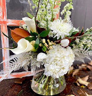 A winter hand-tied bouquet in white hues mixes hydrangea, calla lilies, larkspur, and mums, then is accented with magnolia leaves.