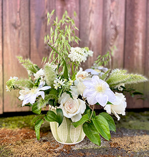 A linear arrangement in white and green combines Princess Miyuki Roses, tweedia, lilies, tulips, clematis, and wild and rustic field grown foliages.