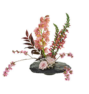 A unique linear floral design uses a kenzan to anchor Quicksand roses, cymbidium orchids, luco foliage, foxglove, brunia, and flowering plum in a slate tray.