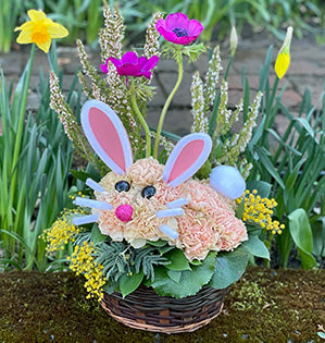 A whimsical and festive bunny design is created from carnations, heather, acacia, anemones, Israeli ruscus and galax leaves.