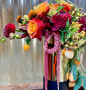 A dramatic elevated design in an analogous color palette features dahlias, rose hips, hanging amaranthus, echinacea pods, asclepias, leucadendron, and passion flower vine.