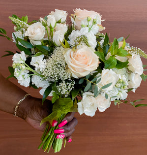 Pale roses in a lovely wedding bouquet clasped by a hand with pink nails.