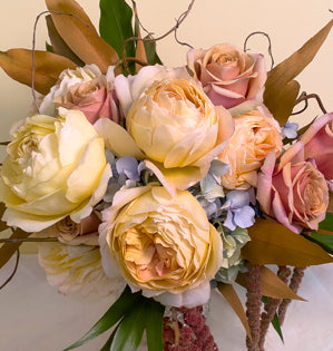 A luscious autumnal-hued bridal bouquet is comprised of Caramel Antike and Golden Mustard roses, hanging amaranthus, grevillea leaves, and a hydrangea nestled in a curly willow armature.