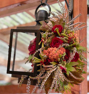 A unique and bold red arrangement full of spray roses, cottage yarrow, calcynia, kangaroo paw, and vine maple decorates a candle lantern inside and out.