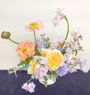 An oval compote garden style design full of Effie garden roses, hyacinth, sweet peas, tweedia, mint, thyme, nerine lilies, and poppies.