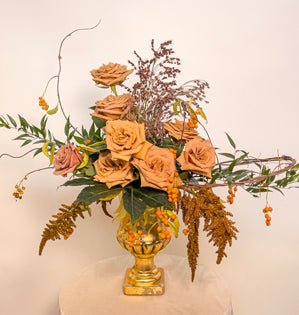 An exquisite design in gold compote, made using Caramella roses, bittersweet, Italian Ruscus, fatsia, amaranthus, and sorghum.